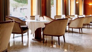 A hotel dining area with round tables, wicker chairs, and large windows with curtains. - Hotel Mozart (Valladolid)