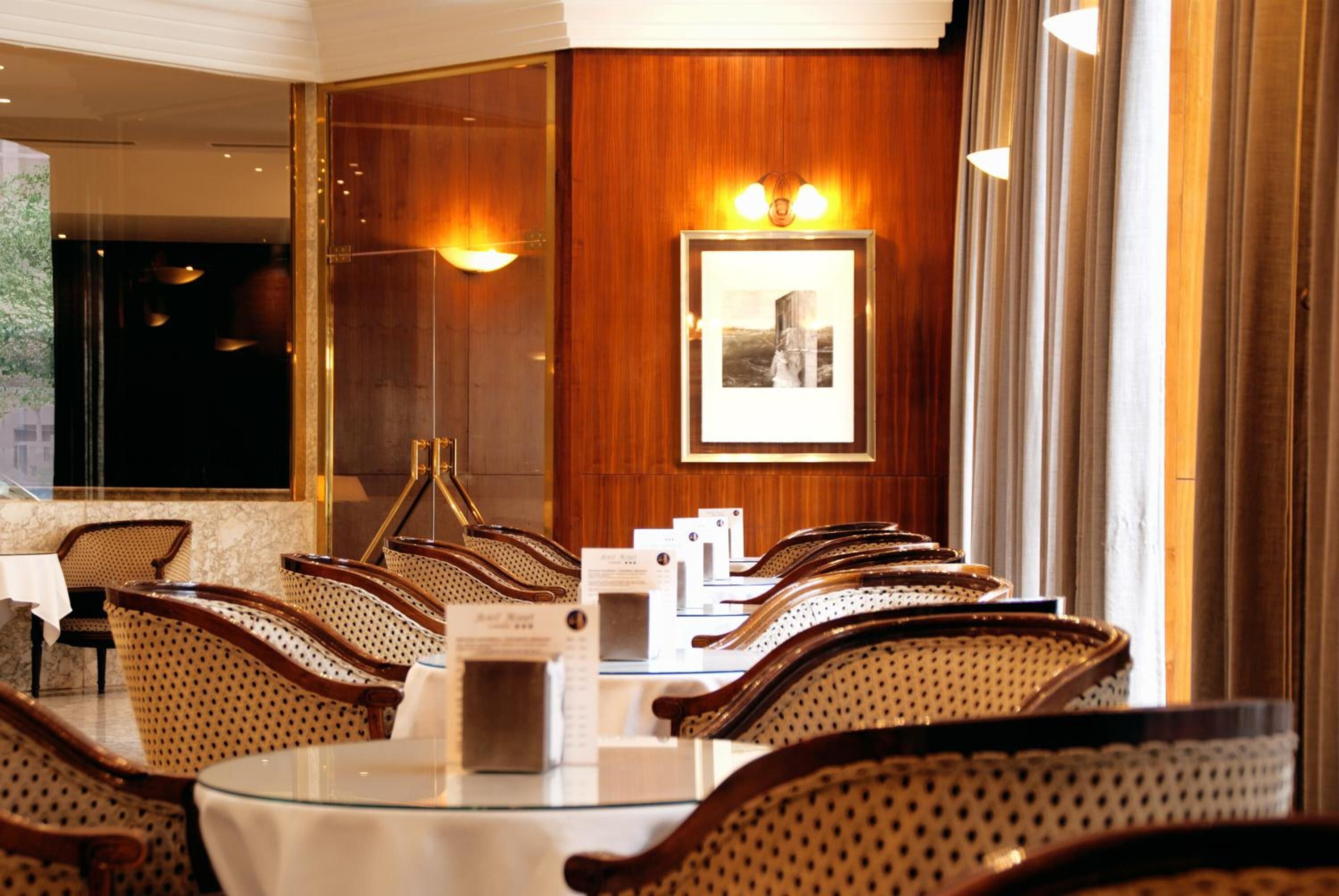 Un espace repas avec des tables rondes et des chaises en osier, un tableau encadré au mur et une vue sur l’extérieur.