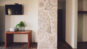 A room with a flat-screen TV mounted on the wall, a wooden table with a plant and a towel, and a patterned wall.