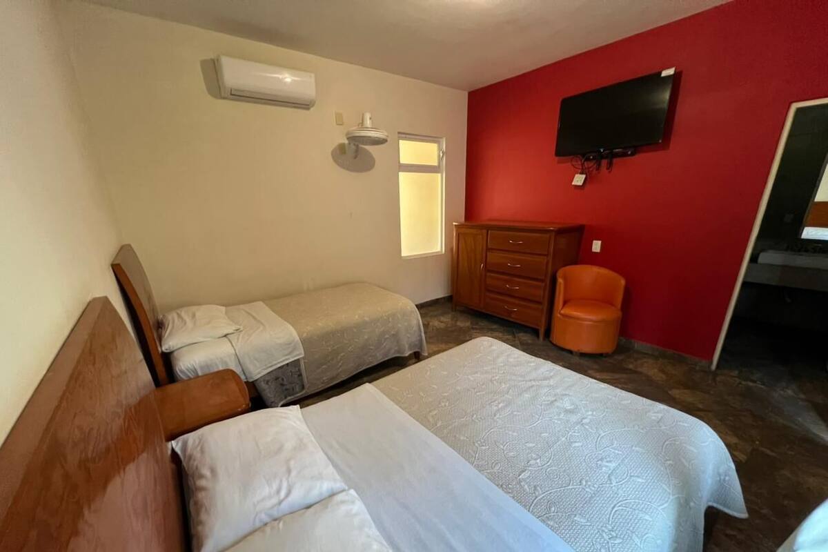 Een kamer met twee bedden, een houten dressoir, een oranje stoel, een televisie aan de muur en een airconditioner.