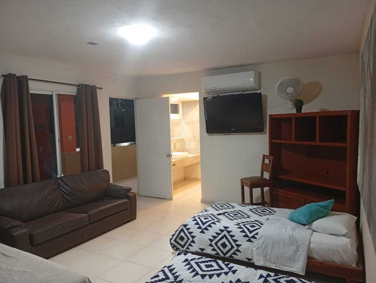 A room with a bed, a sofa, a TV, a fan, and a door leading to a bathroom.