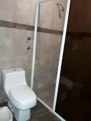 A bathroom with a toilet, a shower enclosure, and a tiled floor.
