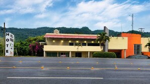 Un hotel con un edificio de dos plantas, un estacionamiento y montañas al fondo.
