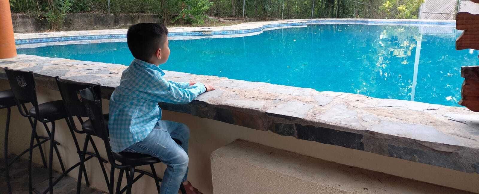 Ett barn sitter vid en pool med trappsteg av sten och ett område med bar.