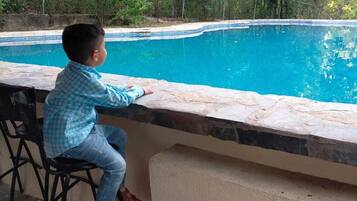 Ett barn sitter vid en pool med trappsteg av sten och ett område med bar.