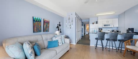 Een woonkamer met een bank, een eethoek met barstoelen, een keuken met een magnetron en een plafondventilator.