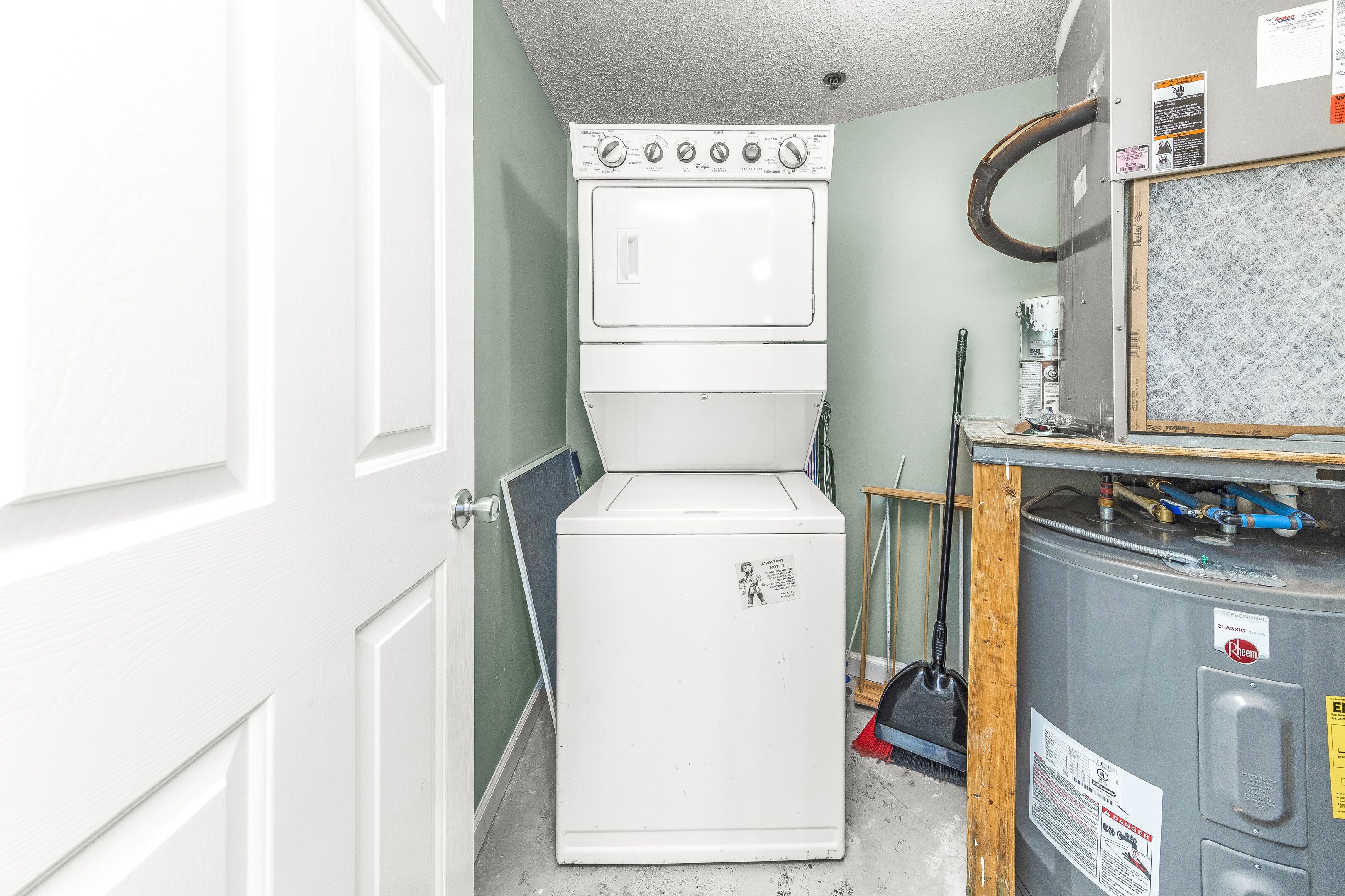 A laundry room with a stacked washer and dryer, a water heater, and a metal cabinet.