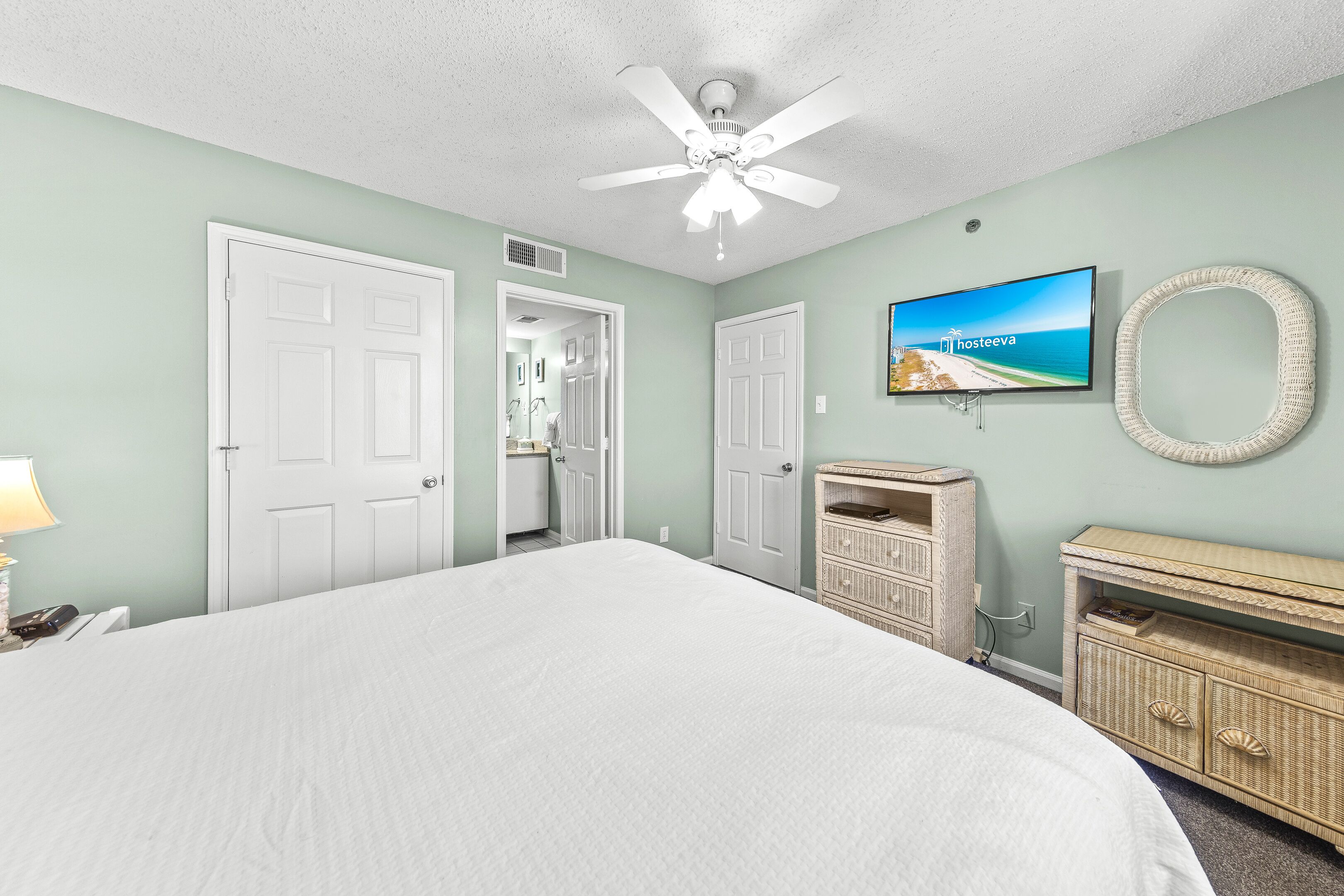 A bedroom with a large bed, a ceiling fan, a television, and a wicker dresser.