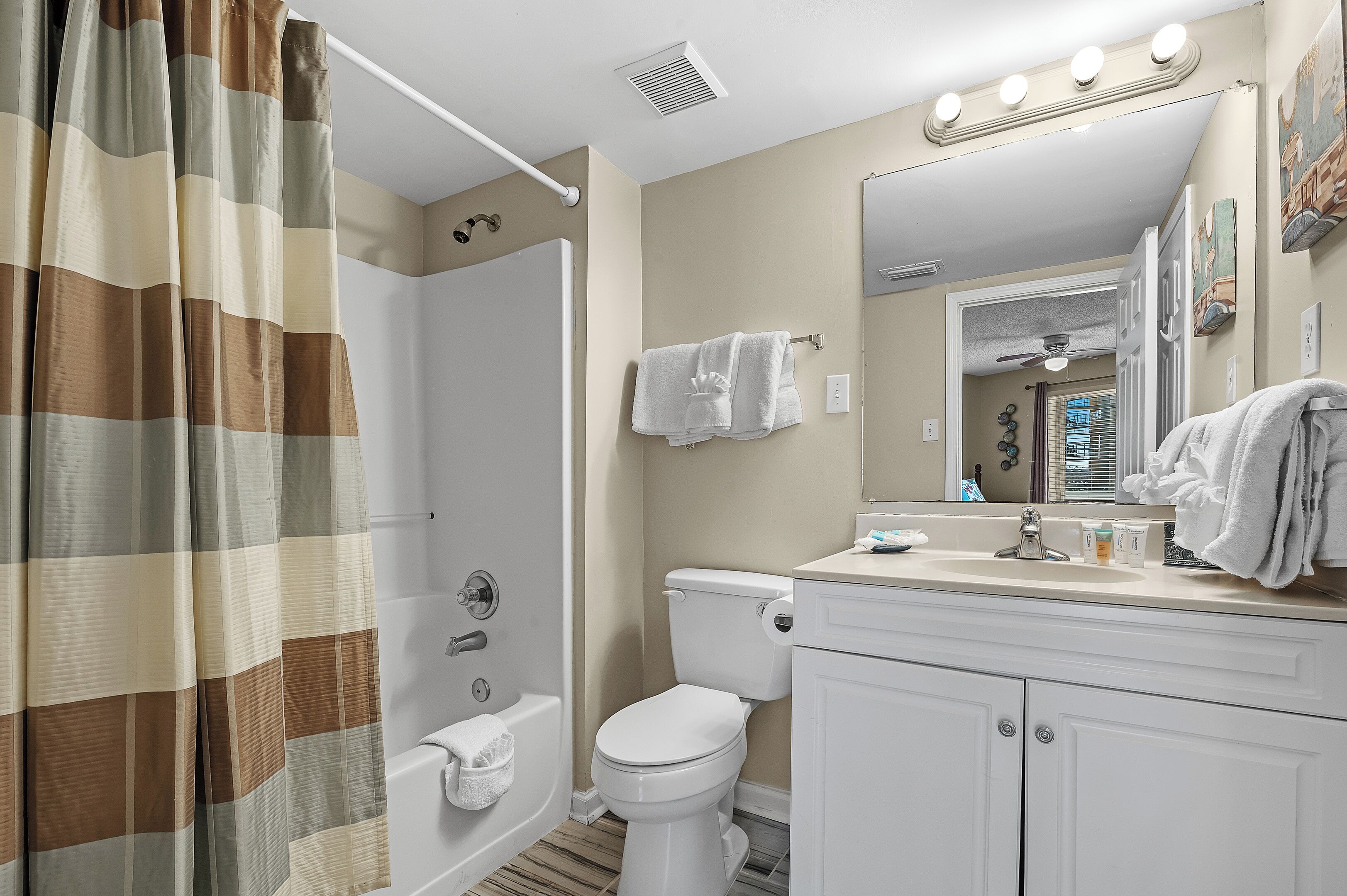 A bathroom with a shower curtain, toilet, sink, and mirror.