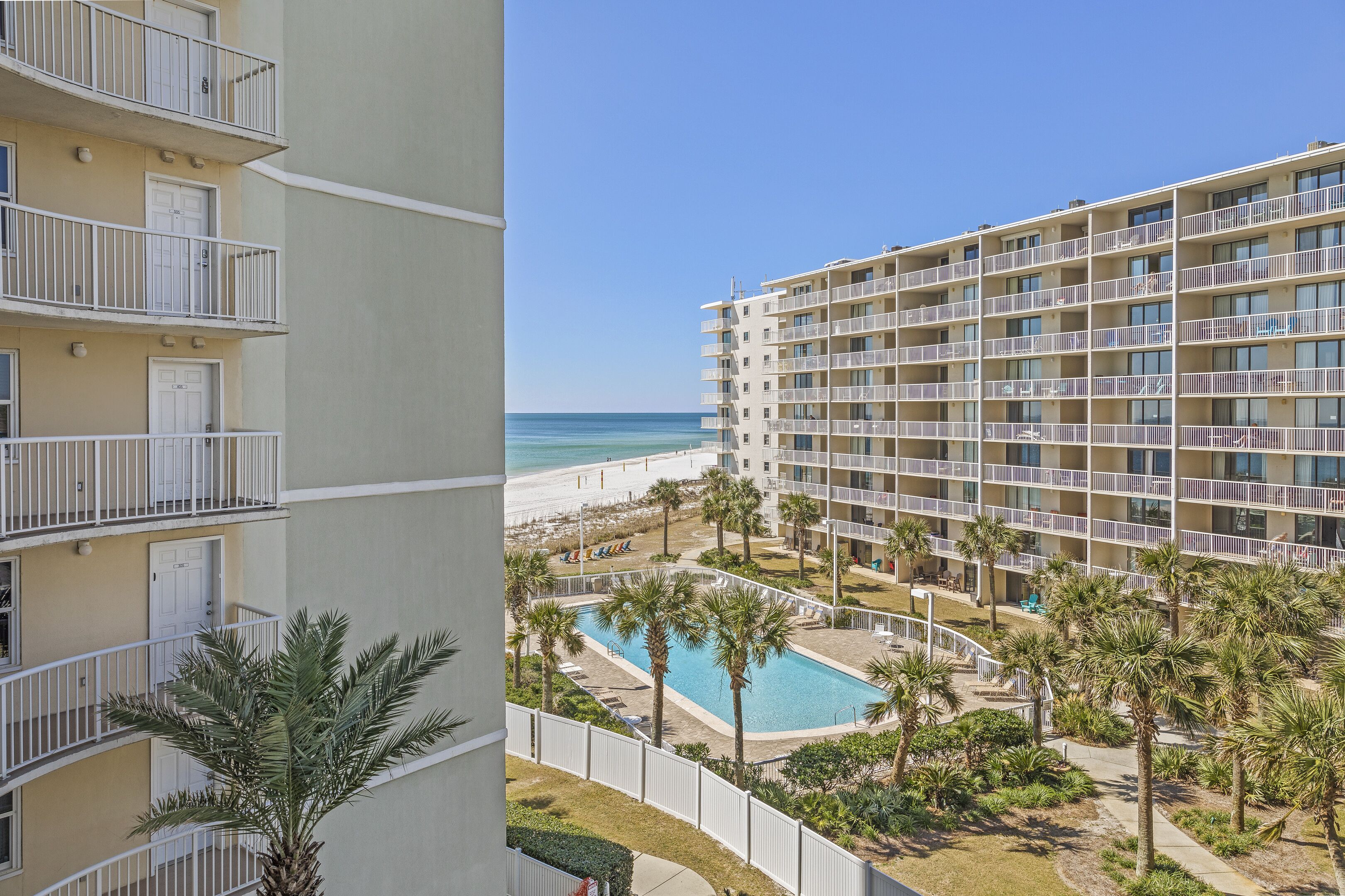 A multi-story hotel with balconies, a swimming pool, and a view of the beach.
