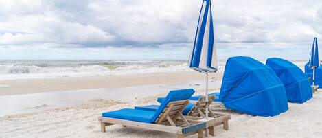 A beach with blue umbrellas and lounge chairs.