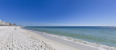 A wide sandy beach with a clear blue sky and calm sea.