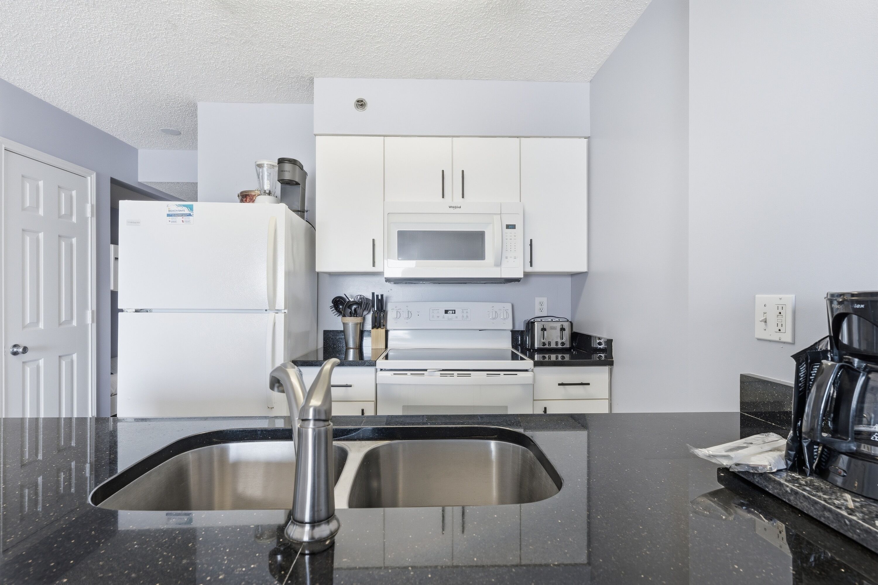 A modern kitchen with a stainless steel sink, white cabinets, a microwave, and a stove.