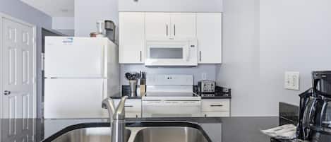 A modern kitchen with a stainless steel sink, white cabinets, a microwave, and a stove.