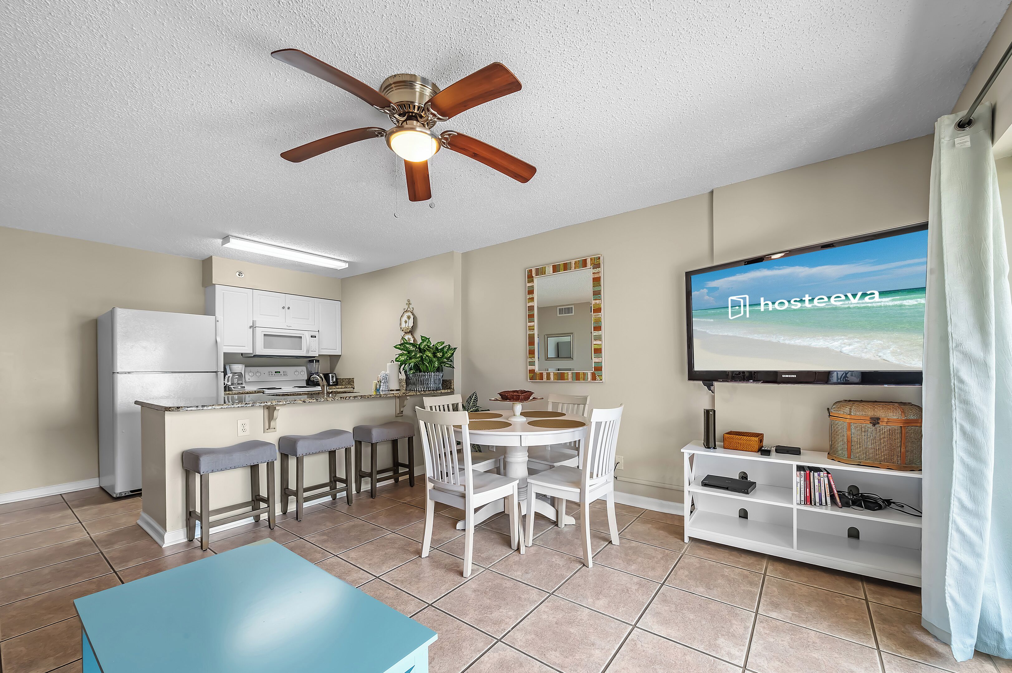 A compact living space with a kitchenette, dining area, and a TV displaying 'hosteeva'.