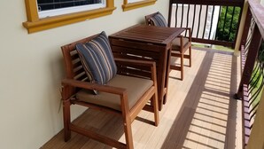 Un área de estar al aire libre con madera, que incluye una mesa, sillas y un banco acolchado, con vistas a un paisaje verde.