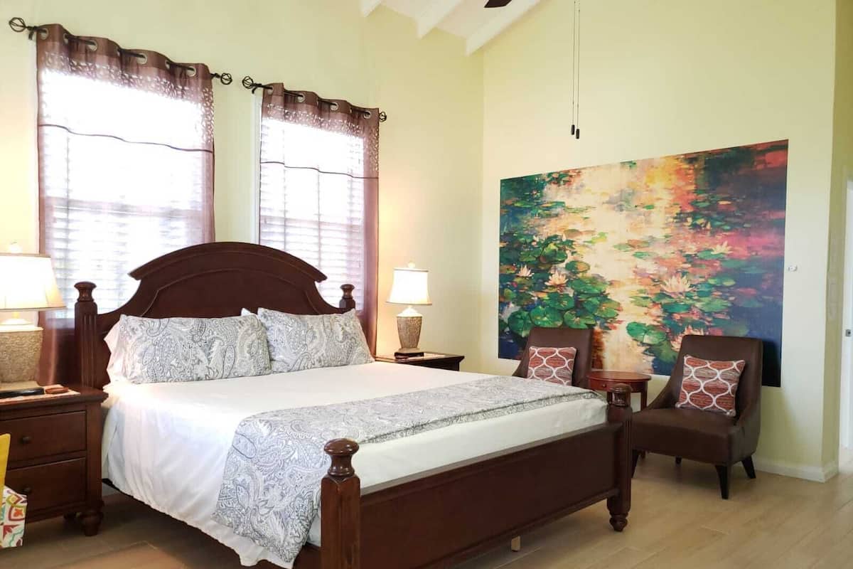 A bedroom with a large bed, two bedside tables, a chair, and a painting on the wall.