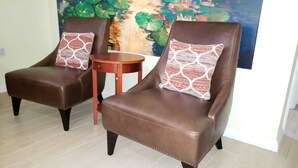 Dos sillones de cuero marrón con cojines estampados, una mesita de madera y un cuadro abstracto colorido al fondo.