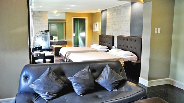 A hotel room with a large bed, a smaller bed, a sofa with cushions, a desk with a chair, and a mirror. - Jardin de Rosal Hotel (Pasig)