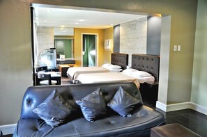 Une chambre d’hôtel avec un grand lit, un plus petit lit, un canapé avec des coussins, un bureau avec une chaise et un miroir.