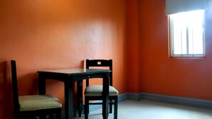 A room with orange walls, a table, two chairs, and a window with blinds. - Jardin de Rosal Hotel (Pasig)