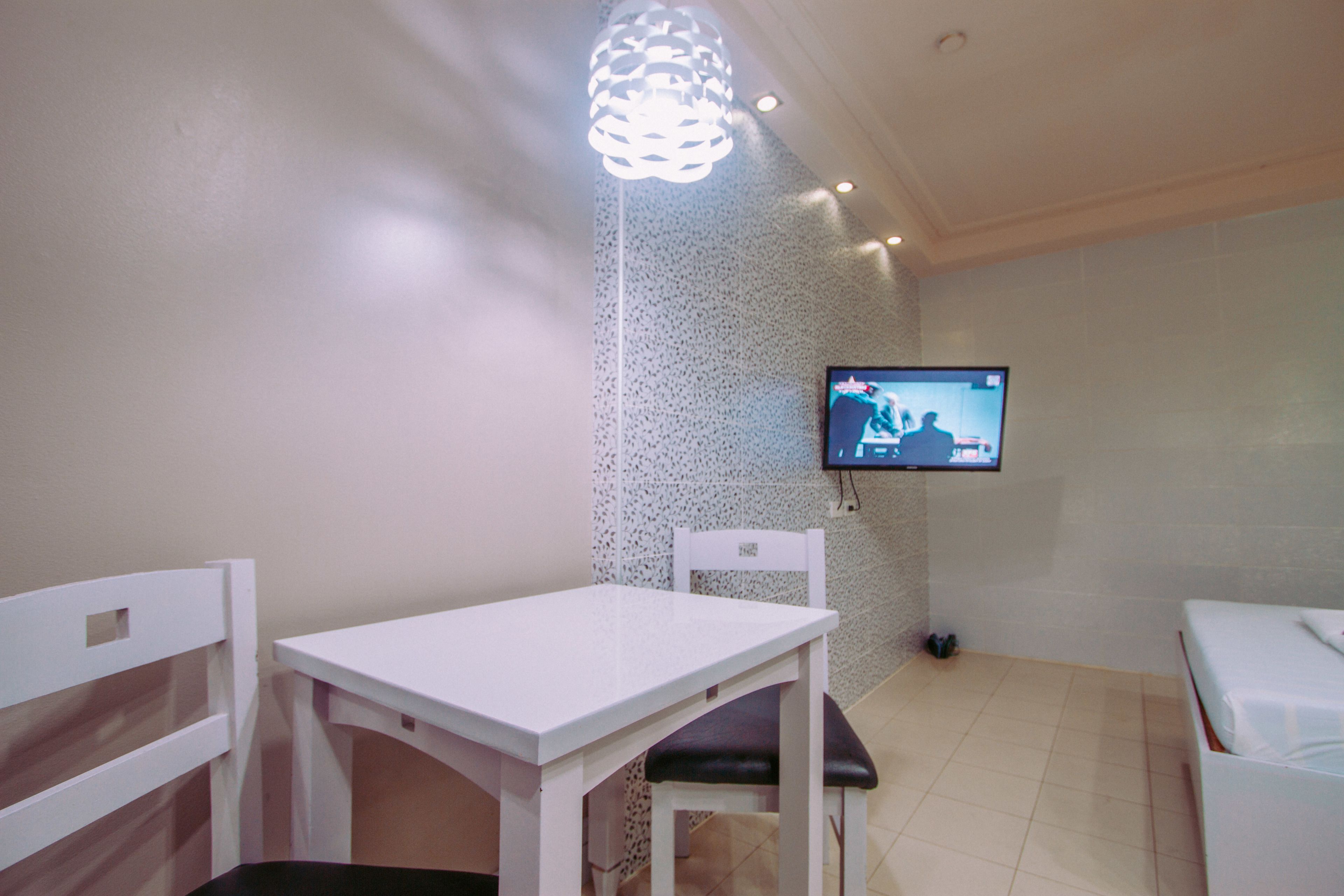 A small, clean room with a white table and chairs, a television mounted on the wall, and a patterned wall.