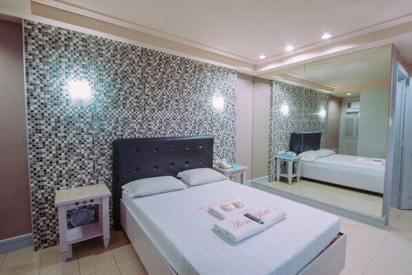 A hotel room with a bed, a nightstand, a mirror, and a tiled wall.