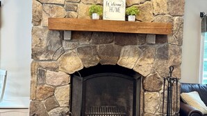 A stone fireplace with a 'Welcome Home' sign, a firewood storage area, and a decorative metal stand. - Upscale Mount Snow/Stratton Area w/Indoor Pool access, short drive to lakes  (West Wardsboro)