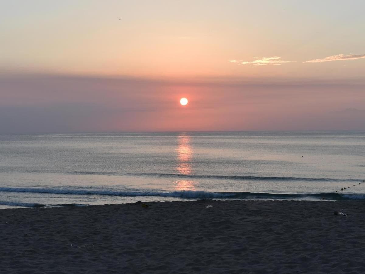 A beach at sunset with calm waves and a clear sky.