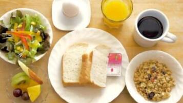 A breakfast setting with a plate of toast, a bowl of cereal, a glass of orange juice, a cup of coffee, a salad, and a fruit bowl.
