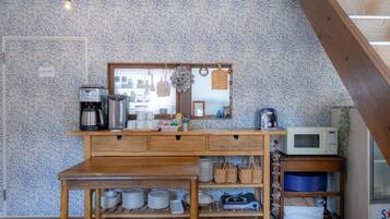 A kitchenette with a wooden table, a coffee maker, a microwave, and a shelf with plates and bowls.