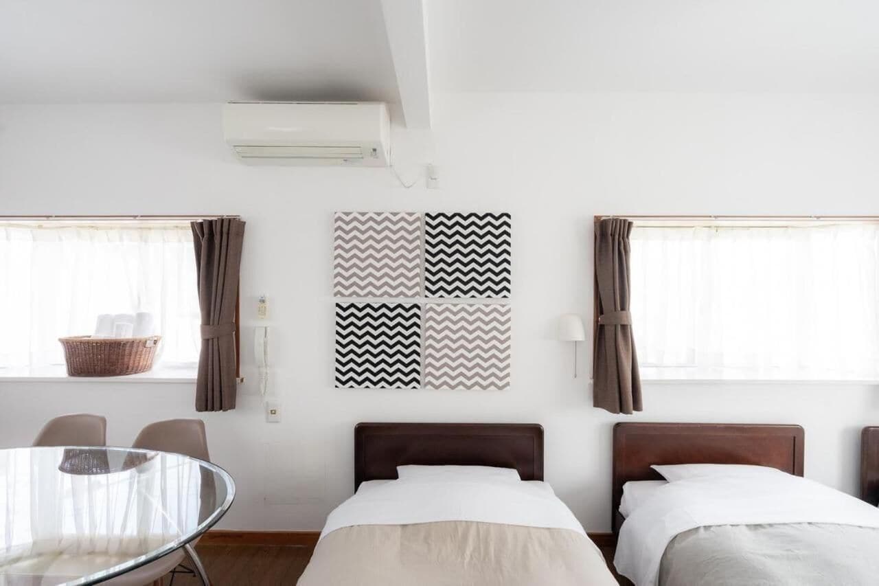 Una habitación de hotel con dos camas, una mesa redonda de vidrio y un aire acondicionado instalado en la pared.