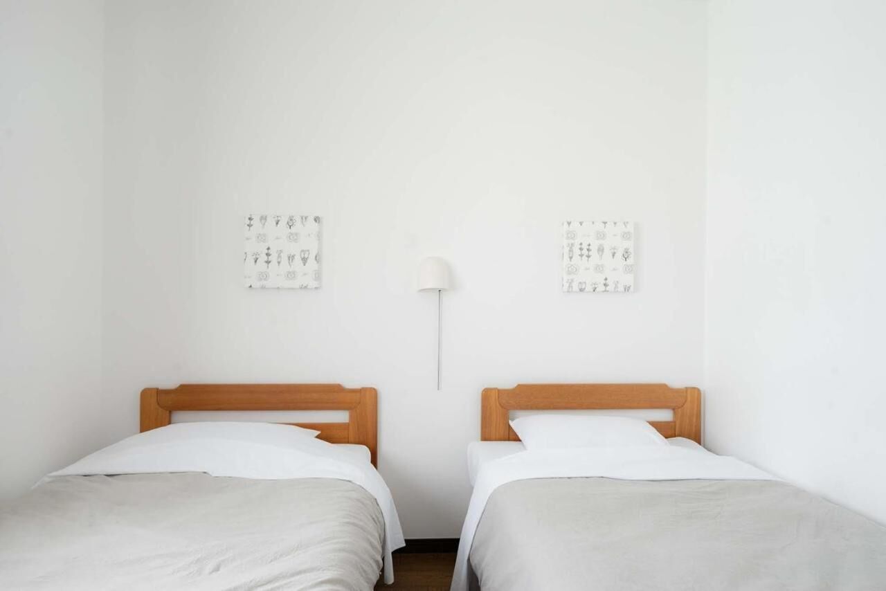 A simple room with two single beds, a white wall, and a wall-mounted lamp.