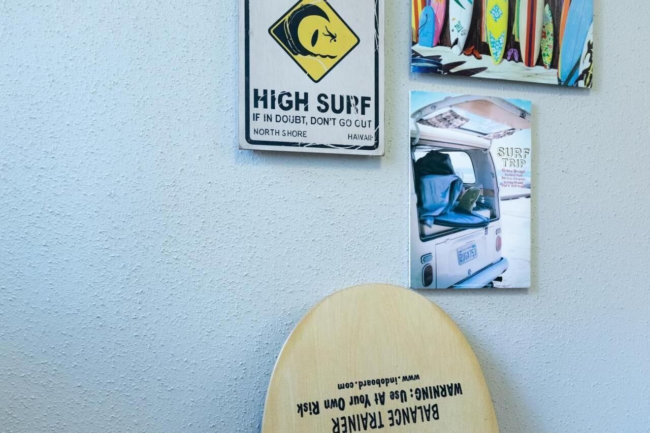 Una pared con un letrero de alerta por oleaje intenso, un cartel promocionando un viaje de surf y una placa de madera.