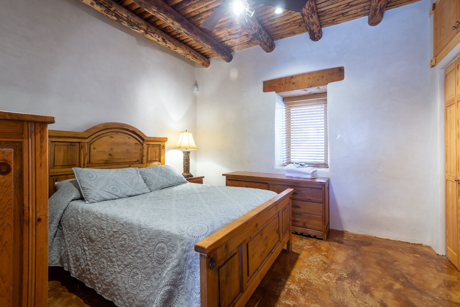A bedroom with a wooden bed, bedside table, and a window with blinds.