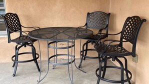 Un patio couvert comprenant une table ronde en métal et quatre chaises, une lanterne et un mur à texture.