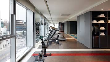 A gym with cardio machines, a towel rack, and a view of the city through large windows.