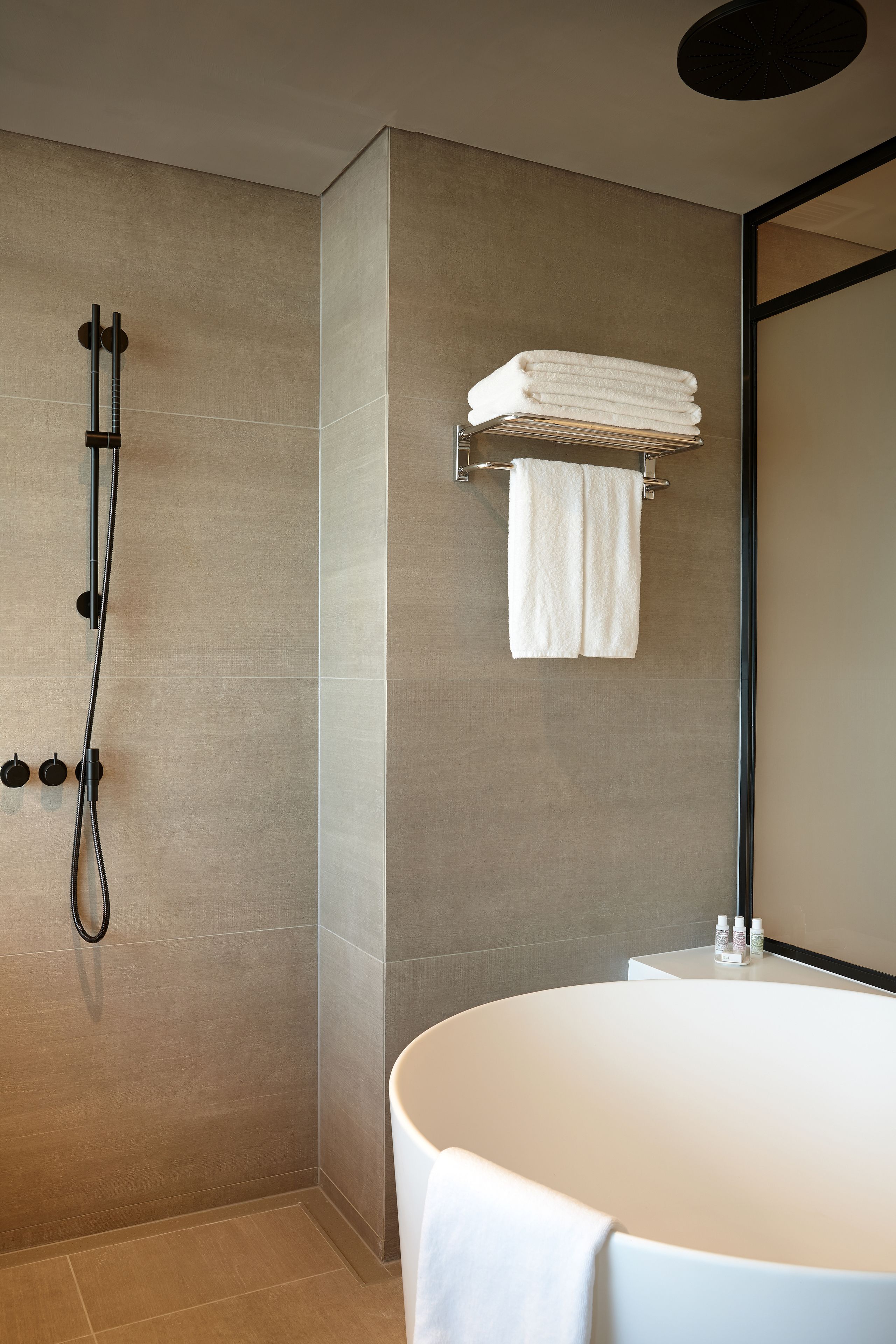 A modern bathroom with a large bathtub, a shower with a handheld showerhead, and a towel rack with folded towels.