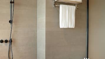 A modern bathroom with a large bathtub, a shower with a handheld showerhead, and a towel rack with folded towels.