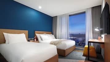 Une chambre d’hôtel avec deux lits, un bureau, une chaise et une grande fenêtre donnant sur la ville.