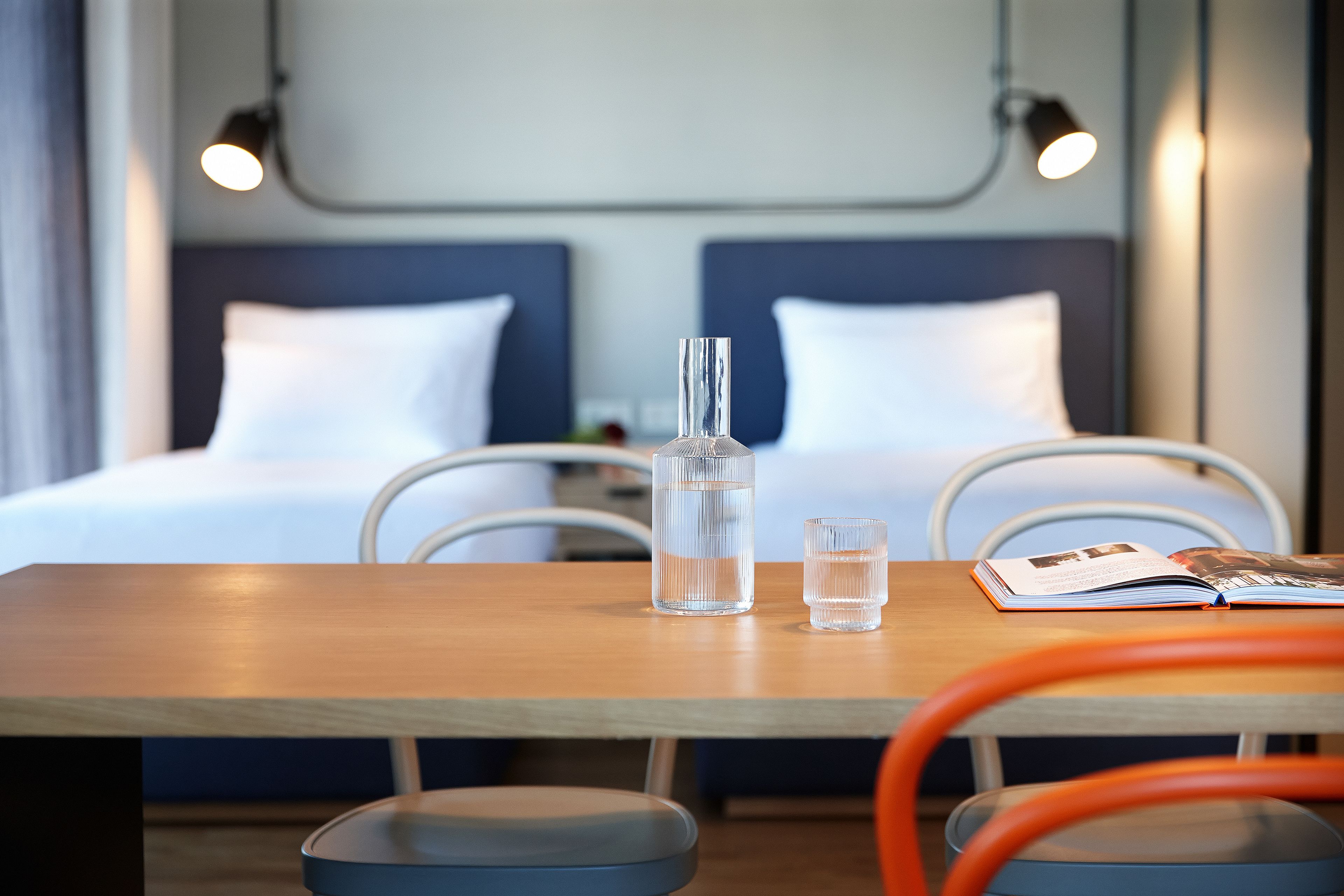 Habitación de hotel con una mesa de madera, dos vasos de agua, un libro y una botella.