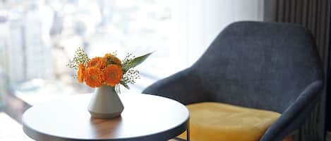 A modern room with a round table, a grey armchair with a yellow cushion, and a vase of orange flowers.
