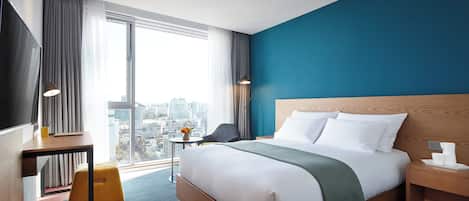 Ett modernt hotellrum med en stor säng, ett skrivbord, en stol och utsikt över staden.