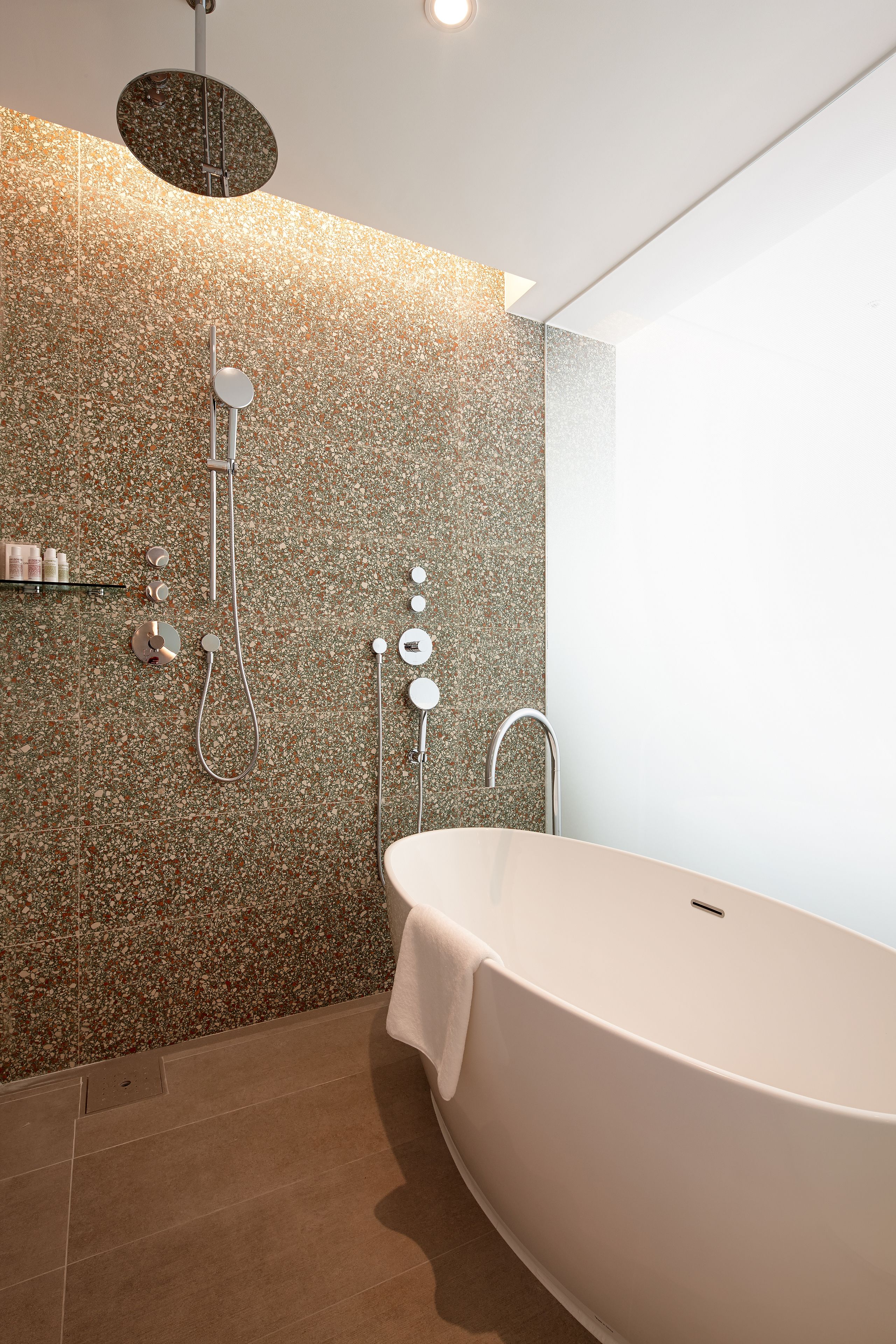 A modern bathroom with a freestanding bathtub, a shower with a circular wall-mounted panel, and a wall-mounted towel rack.