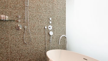 Un baño moderno con una bañera independiente, una ducha con panel circular empotrado y un perchero de pared.