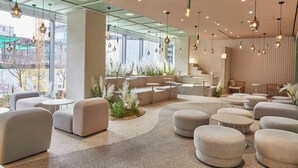 A modern lounge area with seating arrangements, a staircase, and large windows offering views of the outside. - L7 HONGDAE by LOTTE HOTELS (Seoul)