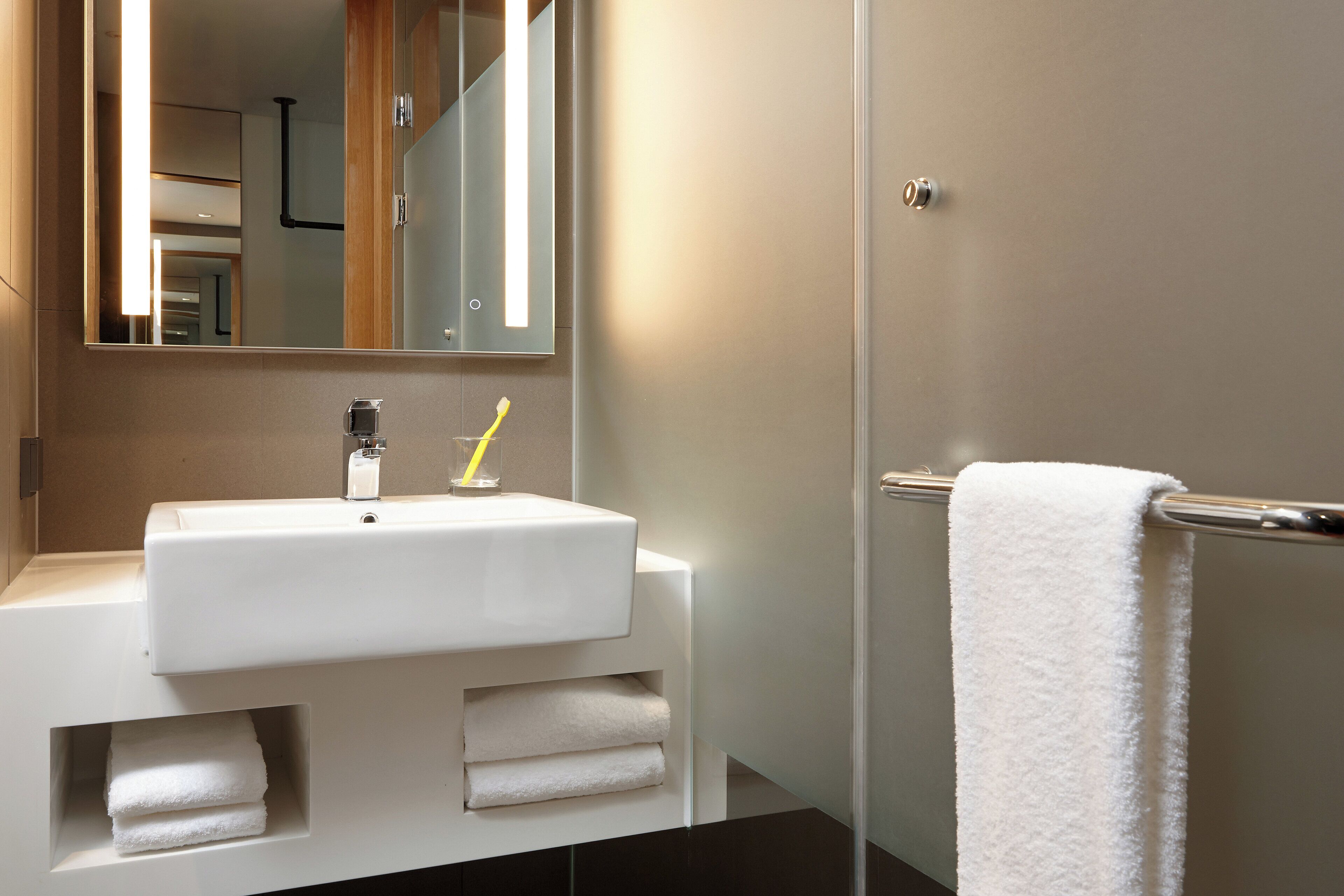 A modern bathroom with a white sink, mirror, and towel rack.