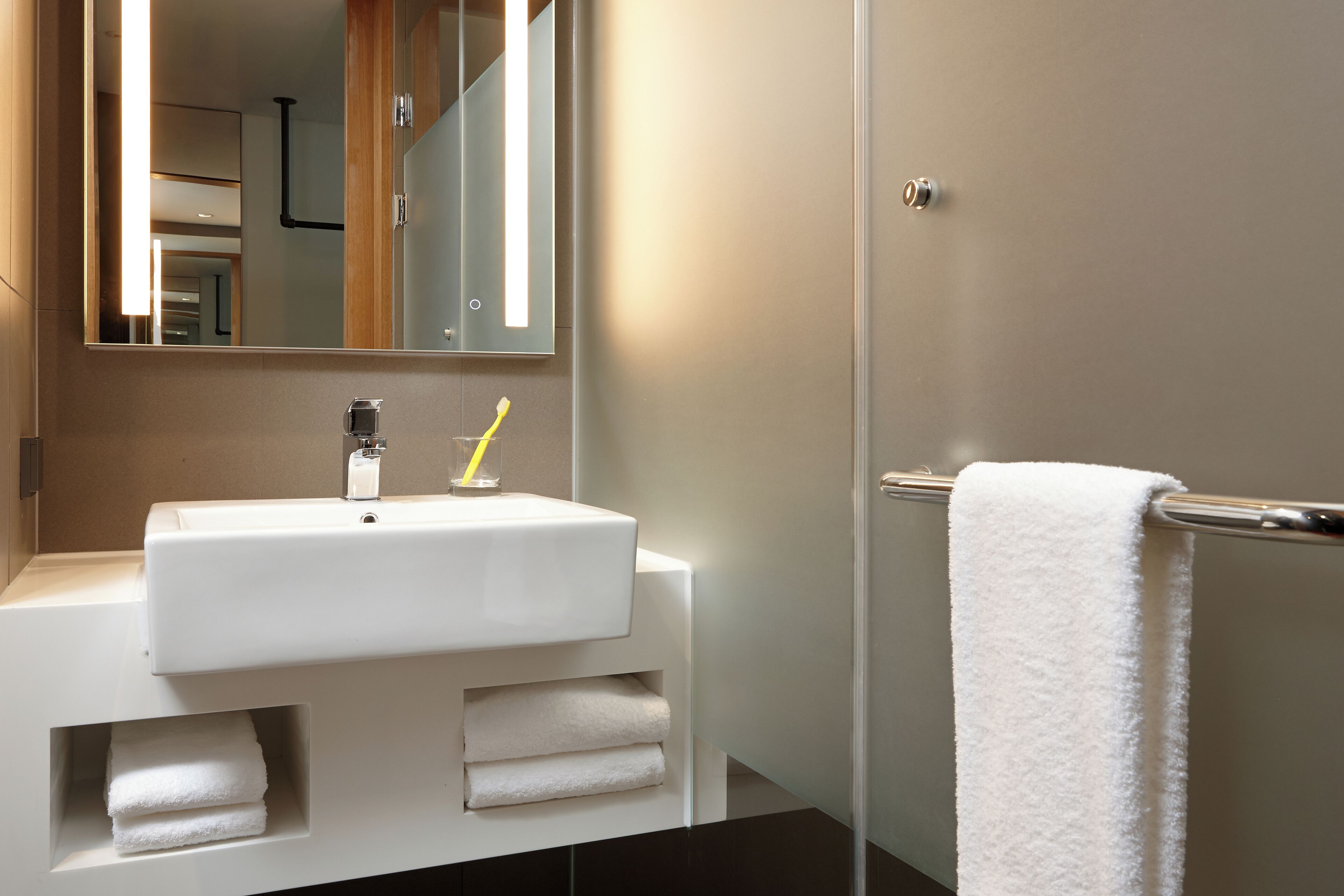 Un baño moderno con un lavamanos blanco, un espejo y un perchero para toallas.