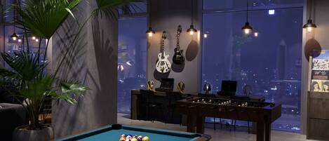 A pool table with pool cues and balls, a foosball table, and guitars hanging on the wall.