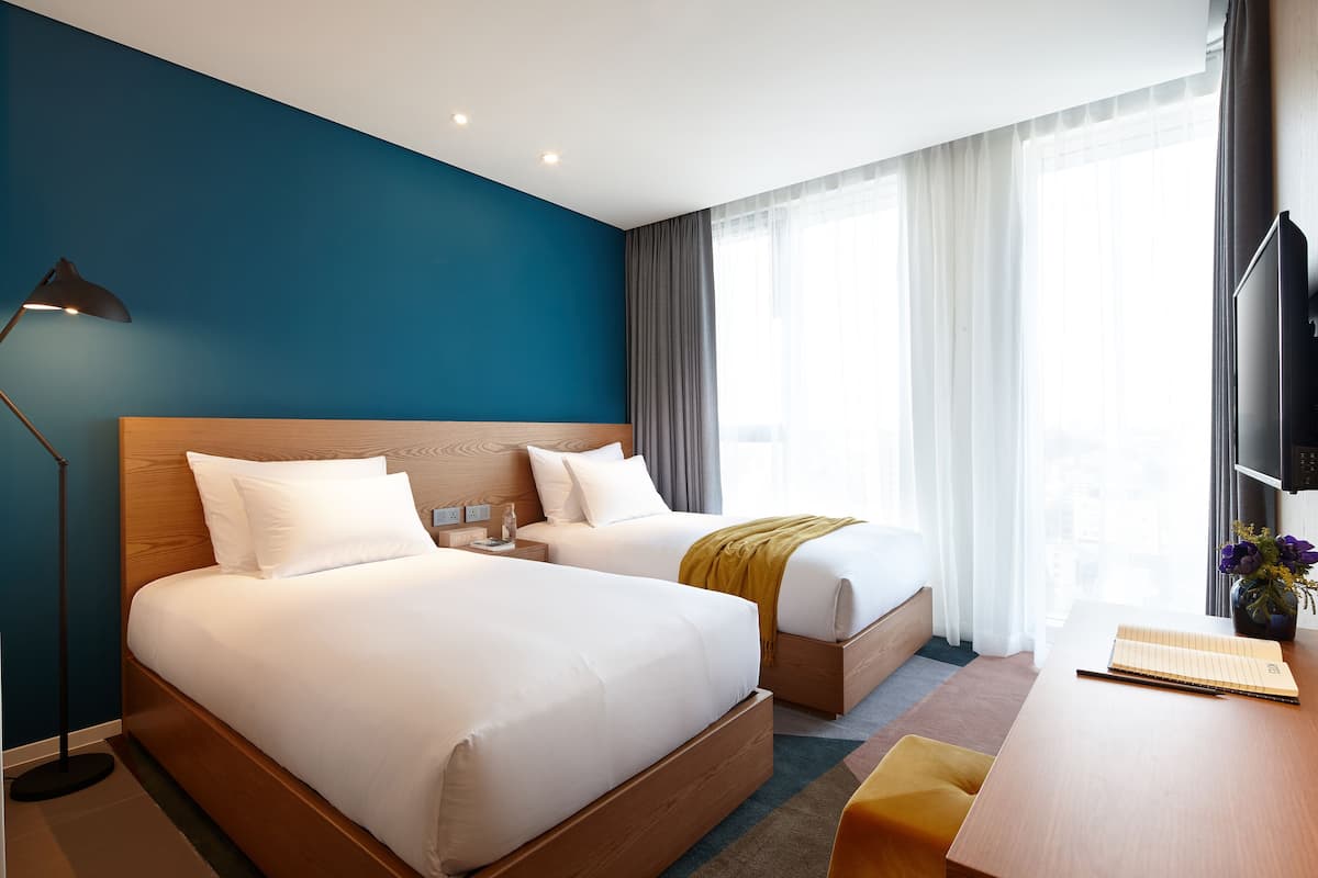 A hotel room with two beds, a desk, a lamp, and a TV.